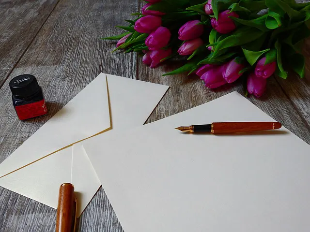 a bouquet of purple tulips next to a white envelope and a pen